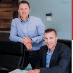 Two men smiling in front of a desk.