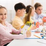 A group of children are sitting at a table making toys.