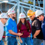 A group of people in hard hats looking at a cell phone.