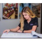 Young woman sitting at desk and reviewing blueprints.