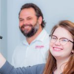 Two people writing on whiteboard and smiling at the camera.